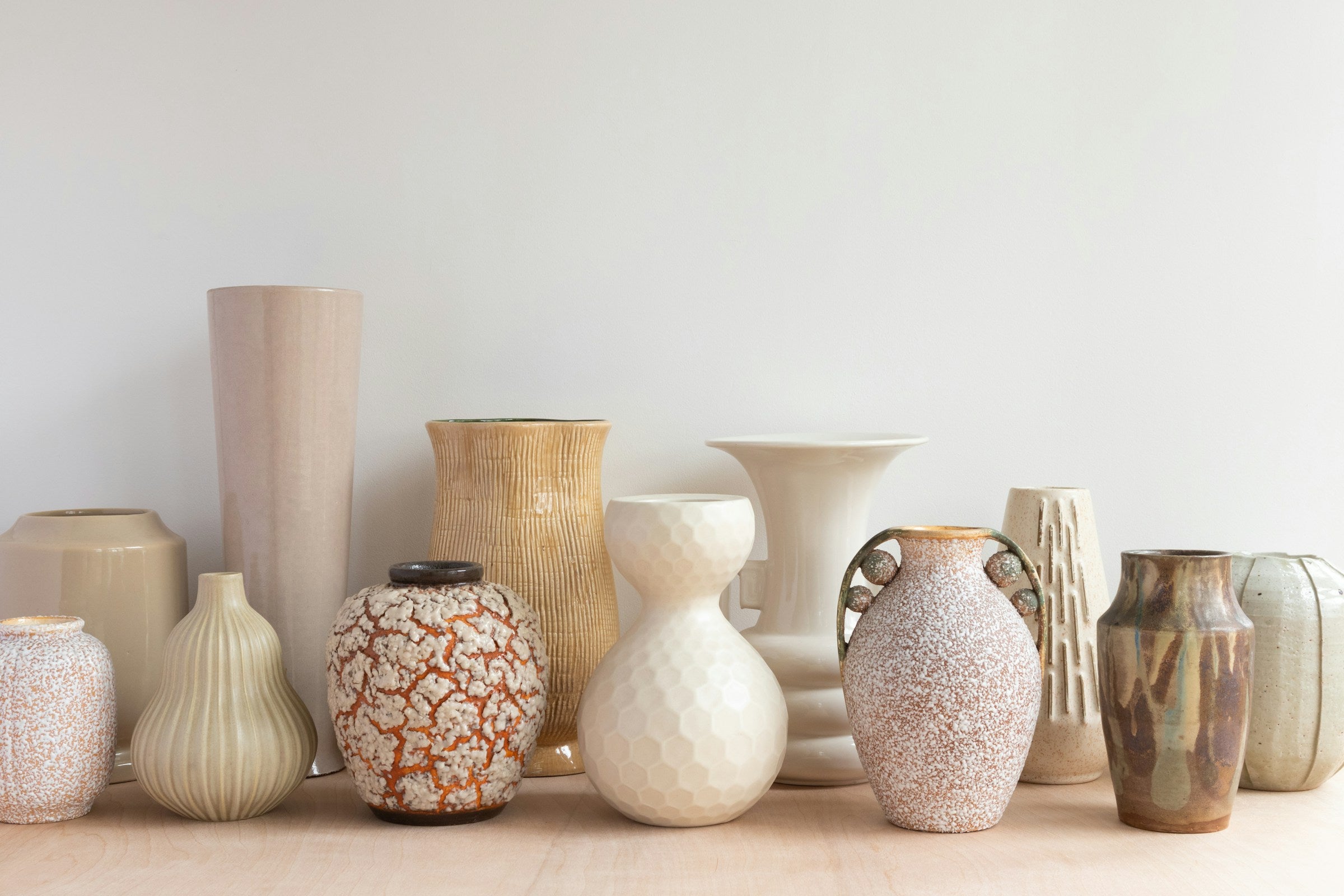 A collection of neutral-toned ceramic vases on a warm white table